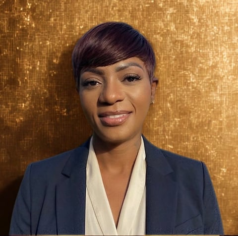 Professional headshot of a woman with short dark hair, wearing a navy blazer over a white shirt, smiling at the camera against a gold sequined background
